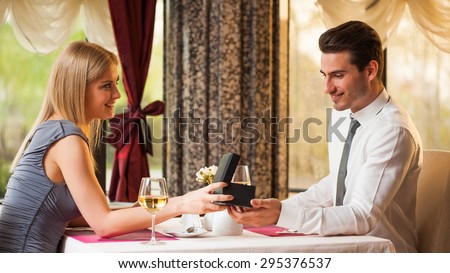 Happy couple at the restaurant, girl is giving present to her boyfriend