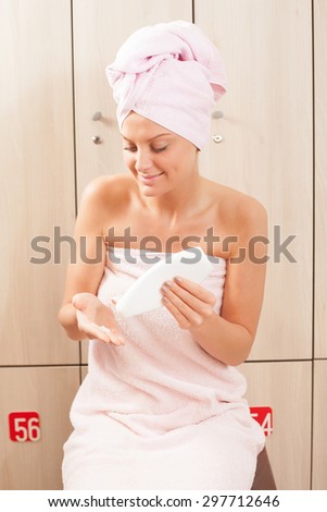 Young woman applying skin cream after shower in gym