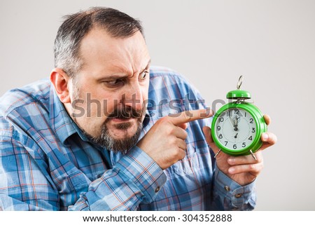Portrait of man holding a clock that shows five to twelve time