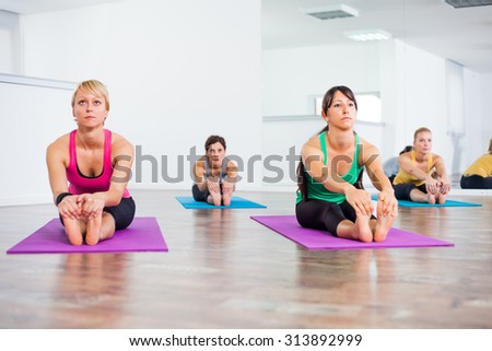 Four girls practicing yoga, Pascimottanasana/Seated Forward Bend pose