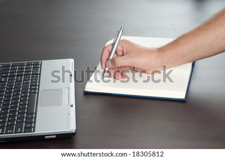 Hand writing on empty notepad,laptop,office desk