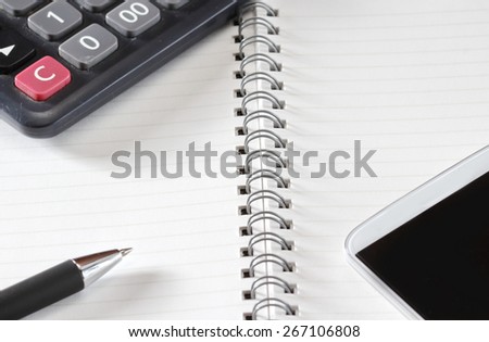 Close up shot of hand held calculator, silver pen and notepad in horizontal layout.