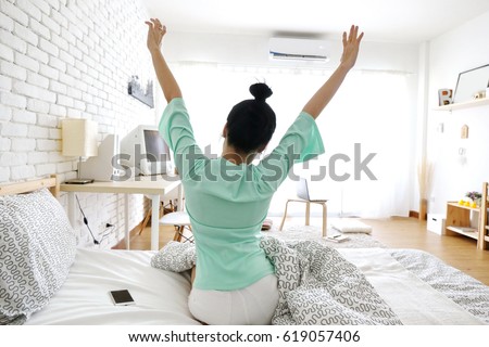 Charming Asian woman sit on bed and hand up wake up on morning in simple white room with air condition. summer season.