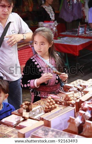 NIGHT BAZAAR MARKET, CHIANG MAI, THAILAND-JANUARY 1:Unidentified young Hmong Hill Tribe girl in traditional costumes sale wood toy in night bazaar market in Chiang Mai, Thailand on January 1, 2012.