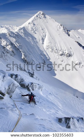 Man with helmet, ice axes and a rope  is climbing in mountains. Winter Polish High Tatra Mountains.