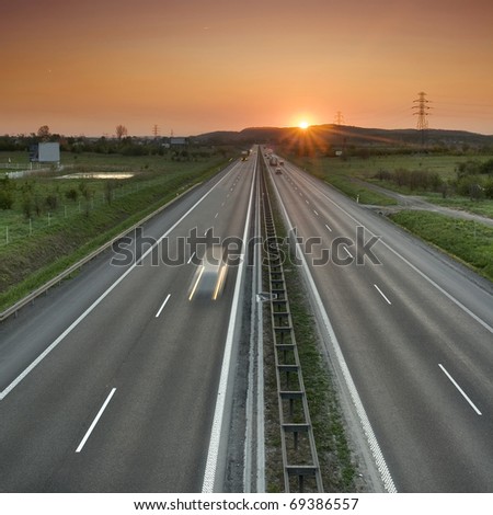 Orange sunset over the two-lane road. A speeding car. Suburbs of Krakow.