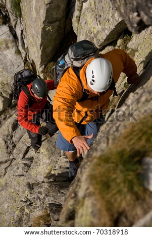 Two scramblers in helmets with backpacks climbing in mountains. Route on the Gerlach in Slovakian High Tatra Mountains.