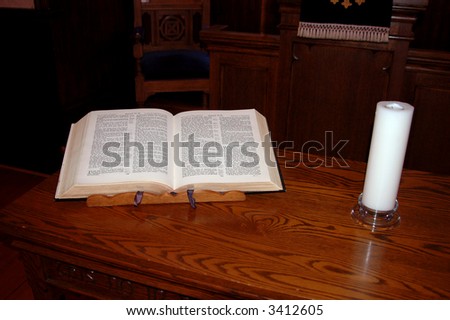 bible on a wooden desk with white pillar candle beside it