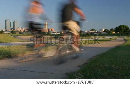 Horizontal image motion shot of couple riding bikes in park with Ft. Worth ,TX in the background