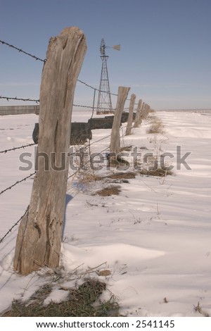 Barbed wire fence with wooden post in a snow covered field