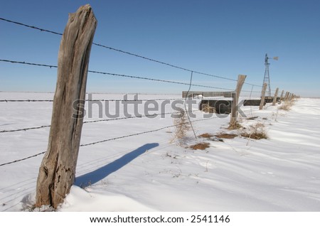 Barbed wire fence with wooden post in a snow covered field