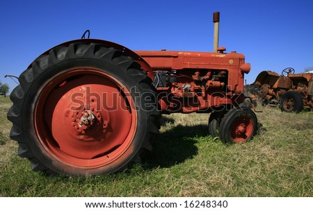 Old red tractor with a big red rear wheel against a deep blue sky