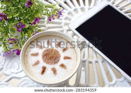 latte art coffee with sun design in white cup and white mobile on white vintage table