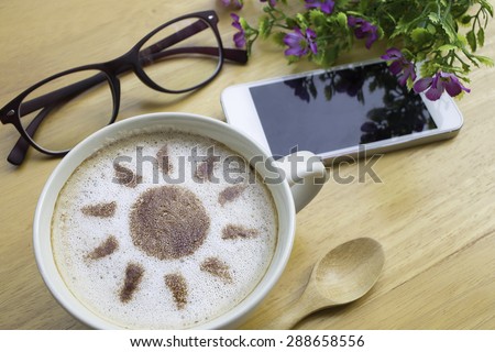 latte art coffee with sun design in white cup and  mobile on wooden vintage table