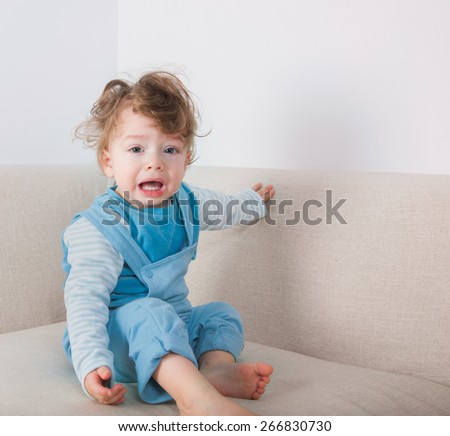 1 year old baby boy crying while sitting on the sofa.