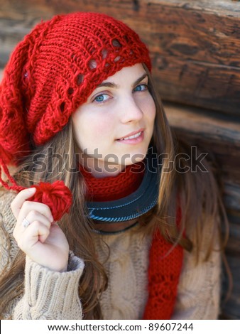 Young girl with ski mask and red hat and scarf against wooden wall.