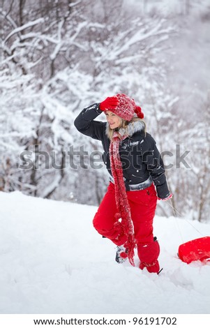 Young woman having fun in the snow, pulling a slay on the slope.