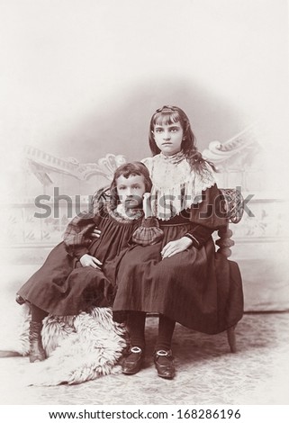 USA - IOWA - CIRCA 1895 - A vintage photo of two young sisters dressed in Victorian style dresses. They are both sitting in a chair. A photo from the Victorian era. CIRCA 1895