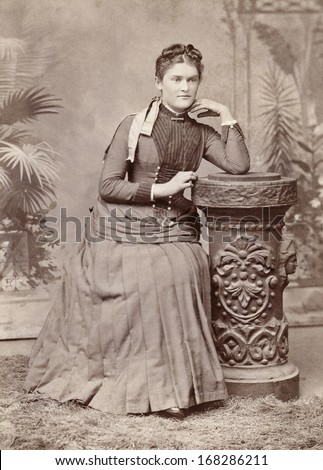 USA - IOWA - CIRCA 1885 - A vintage photo of a young beautiful woman dressed in a Victorian bustle style dress. She is posed sitting in a chair. A photo from the Victorian era. CIRCA 1885