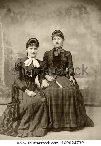 USA - NEW YORK - CIRCA 1890 - A vintage antique photo of two young women sitting in fashionable clothing. Both women are dressed in a Victorian style dress. A photo from the Victorian era. CIRCA 1890