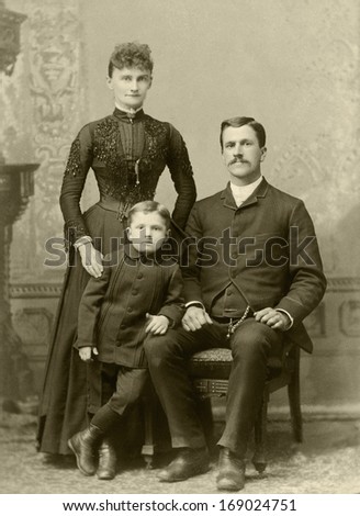 US - OREG0N - CIRCA 1885 - A vintage antique photo of a family of three. The mother is standing behind her young son with the father sitting in a chair. A photo is from the Victorian era. CIRCA 1885