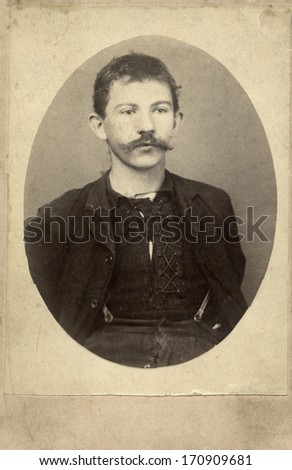 USA - KANSAS - CIRCA 1870 A vintage photo of a poor young pioneer man with a mustache. He is wearing a tattered lace up shirt with jacket and suspenders. Photo is from the Victorian era. CIRCA 1870
