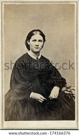 USA - CONNECTICUT - CIRCA 1865 - A vintage Cartes de visite photo of young pioneer woman sitting in chair. She is dressed in hoop skirt dress.  Photo from the Civil War Victorian era. CIRCA 1865