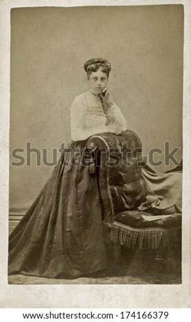 CANADA - ONTARIO - CIRCA 1870 - A vintage Cartes de visite photo of a young woman standing and leaning on a chair. She is dressed in Victorian style dress.  Photo from the Victorian era. CIRCA 1870