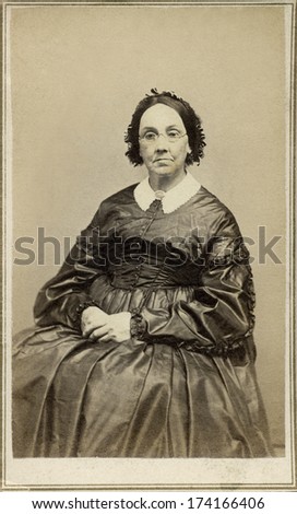 USA - NEW YORK - CIRCA 1865 - A vintage Cartes de visite photo of older pioneer woman in chair. She is dressed in hoop skirt dress and wearing eye glasses.  Photo from the Civil War Victorian era.