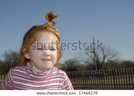 A little girl with her hair in a pony tail grinning