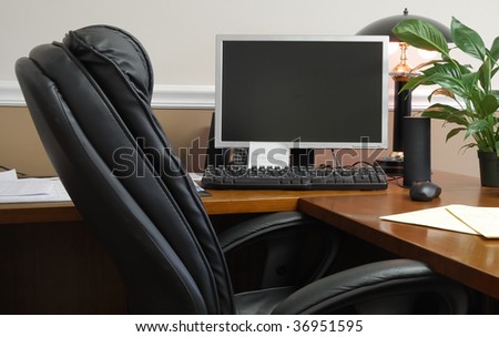 An office desk with leather office chair and a computer monitor as well as keyboard on the desk.