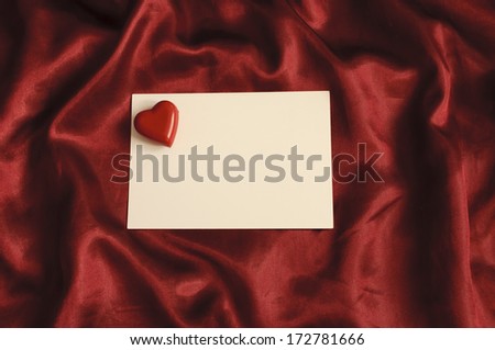 Love note, blank piece of paper and a red heart, on a red satin sheet