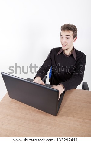 surprised young man with laptop smiling at a desk in an office chair