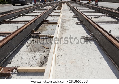 new railway tracks near a busy street in a city with cars on the road