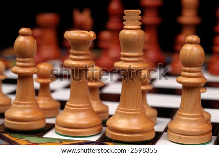 Light colored wooden chess pieces (king, queen, and bishops) in sharp focus with dark pieces out of focus across the chess board