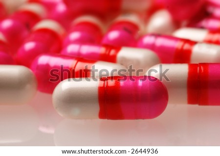 Pink, red, and white medicine capsules. One capsule in foreground in sharp focus.
