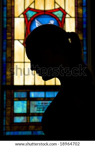 Young woman in prayer silhouetted in front of a stained glass window