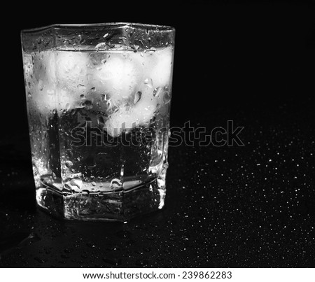 Glass of Water with Ice Cubes on black reflective background with Water Drops
