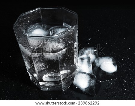 Glass of Water with Ice Cubes on black reflective background with Water Drops