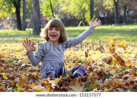 happy little girl throw leaves in autumn park