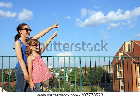 happy teenage and little girl pointing on sky