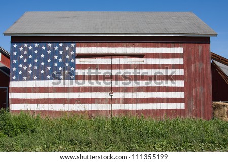 The American flag is painted on the front of an old barn.