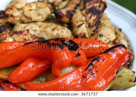 Grilled Peppers: the focus is on the fresh orange and green peppers which have been grilled on the barbecue. The grilled chicken is out of focus.