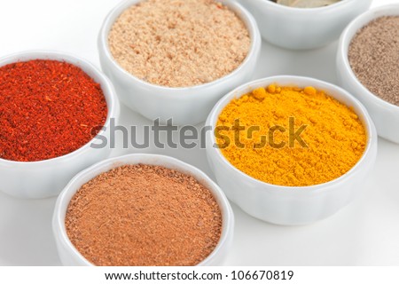 Different spices in white bowls isolated on white background. Paprika, Curry, Black Pepper, Ginger, Cinnamon, Bay Leaves.
