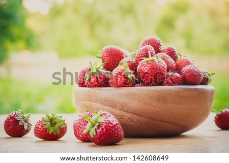 Old wooden bowl filled with succulent juicy fresh ripe red strawberries on an old wooden textured table top / Close-up of strawberries in vintage wooden bowl on wooden table