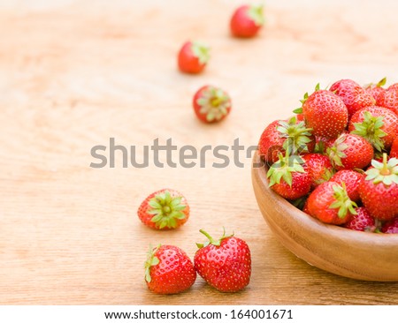 Old wooden bowl filled with succulent juicy fresh ripe red strawberries on an old wooden textured table top