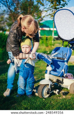 Young Woman Mother Wears Jacket On Son Little Boy On Walk In Spring. Outdoor Portrait