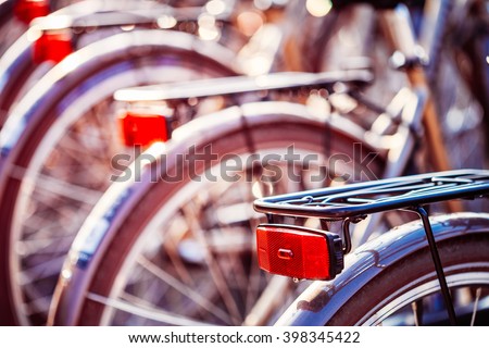 Close Up Of Bicycles On Parking In European City. Sunlight Sunshine Through Spokes Of Wheel. Close Up Of Bike Red Light, Lamp In Bokeh Background.