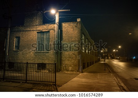 Dark urban city street and alleyway corner with an industrial warehouse factory and an urban road leading to a vintage bridge in Chicago at night.