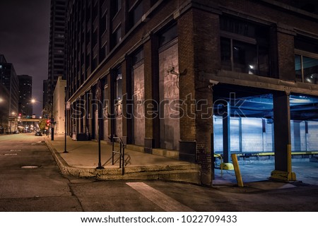 Dark city downtown street corner with an industrial warehouse loading dock at night.